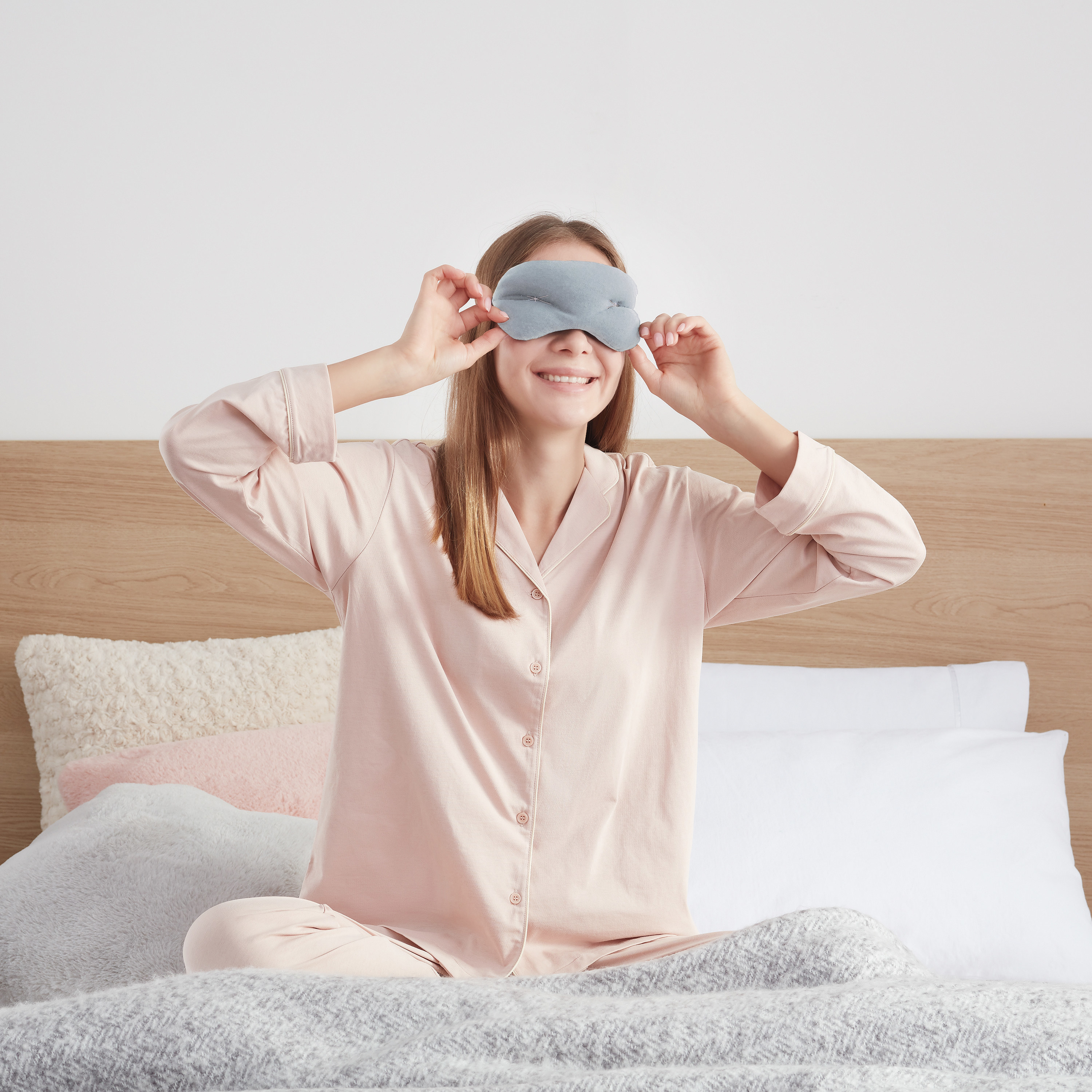 Model wearing pink pajamas and gray eye mask in bed