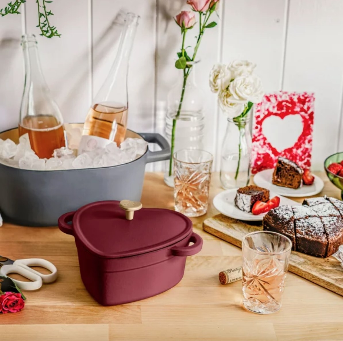 Red heart-shaped dutch oven on table with desserts and wine on ice