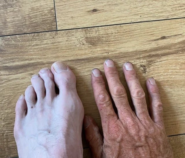 A very pale foot and a very suntanned hand that has lots of wrinkles