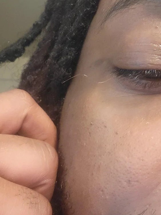 A person holding out a very long, curly, blonde eyelash from their eye