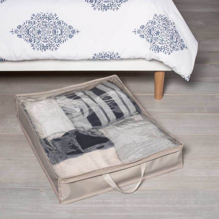 the grey storage bag with sweaters on the floor next to a bed