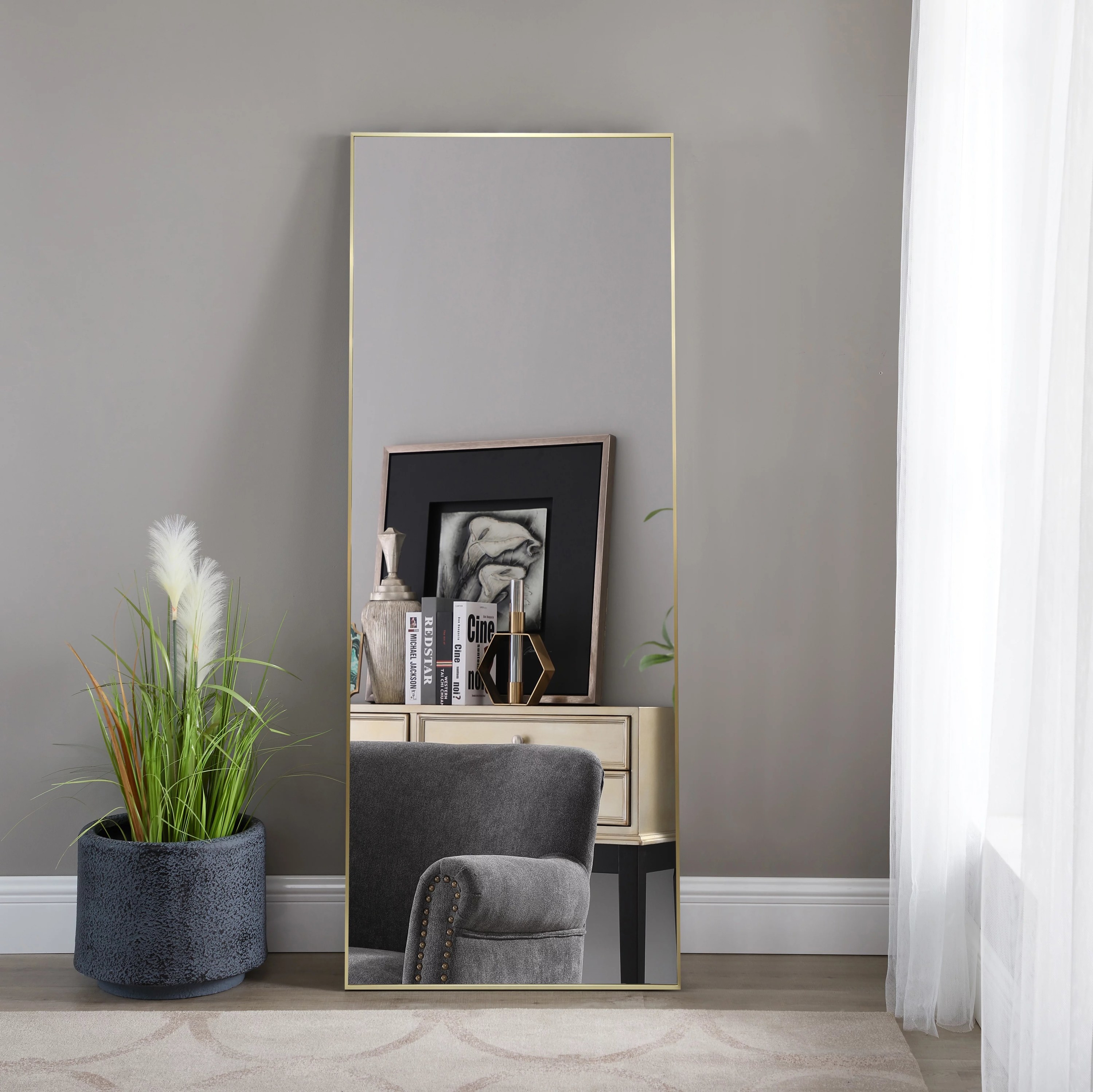 The standing mirror in gold next to a potted plant