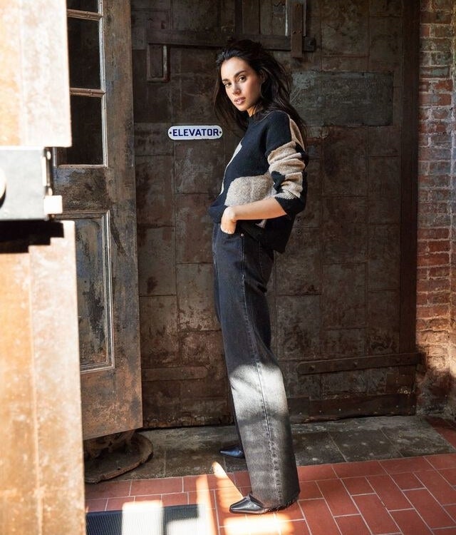 a side view of someone standing outside wearing the jeans with a knit sweater