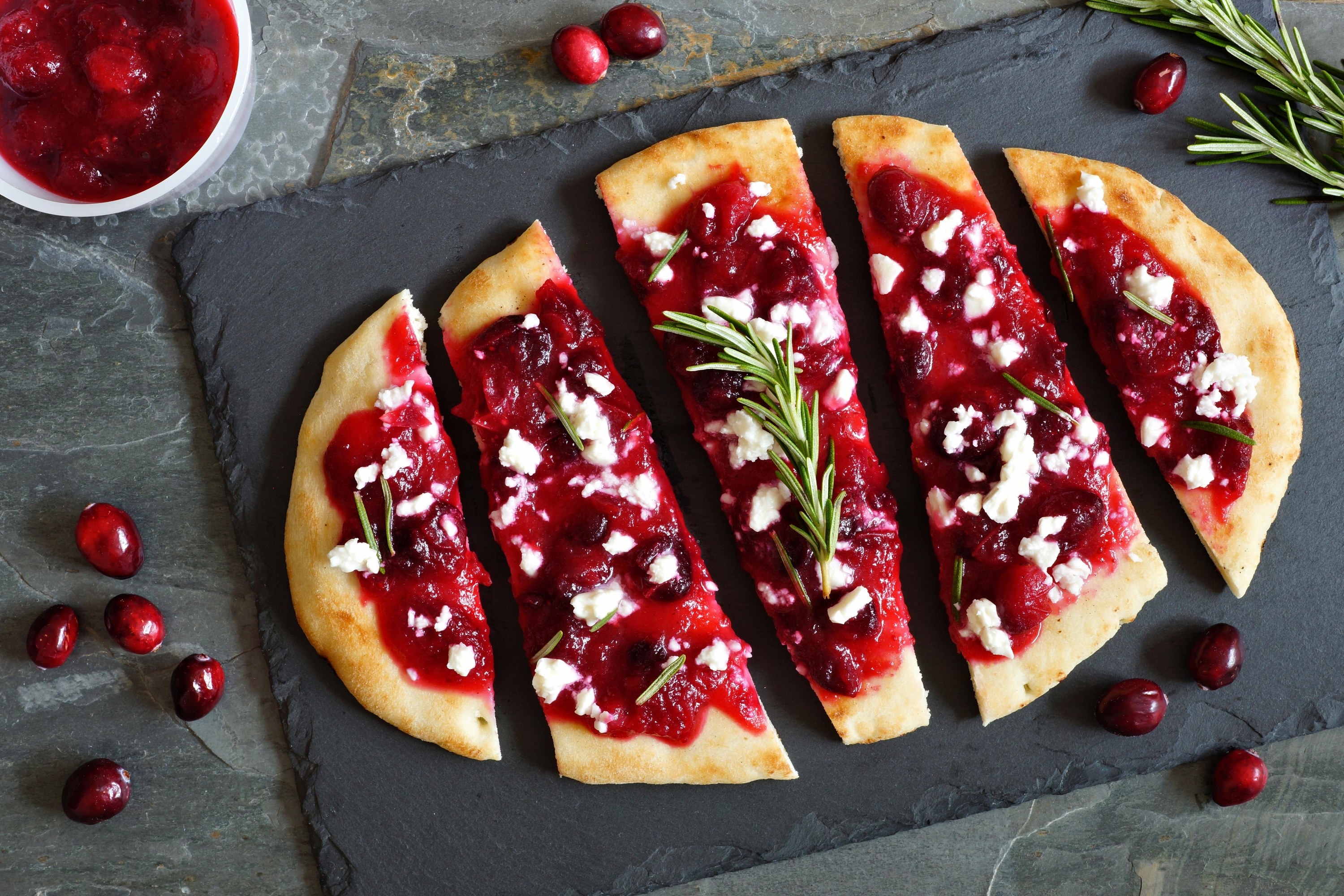Holiday flatbread appetizer with cranberries and goat cheese, overhead scene on a slate background
