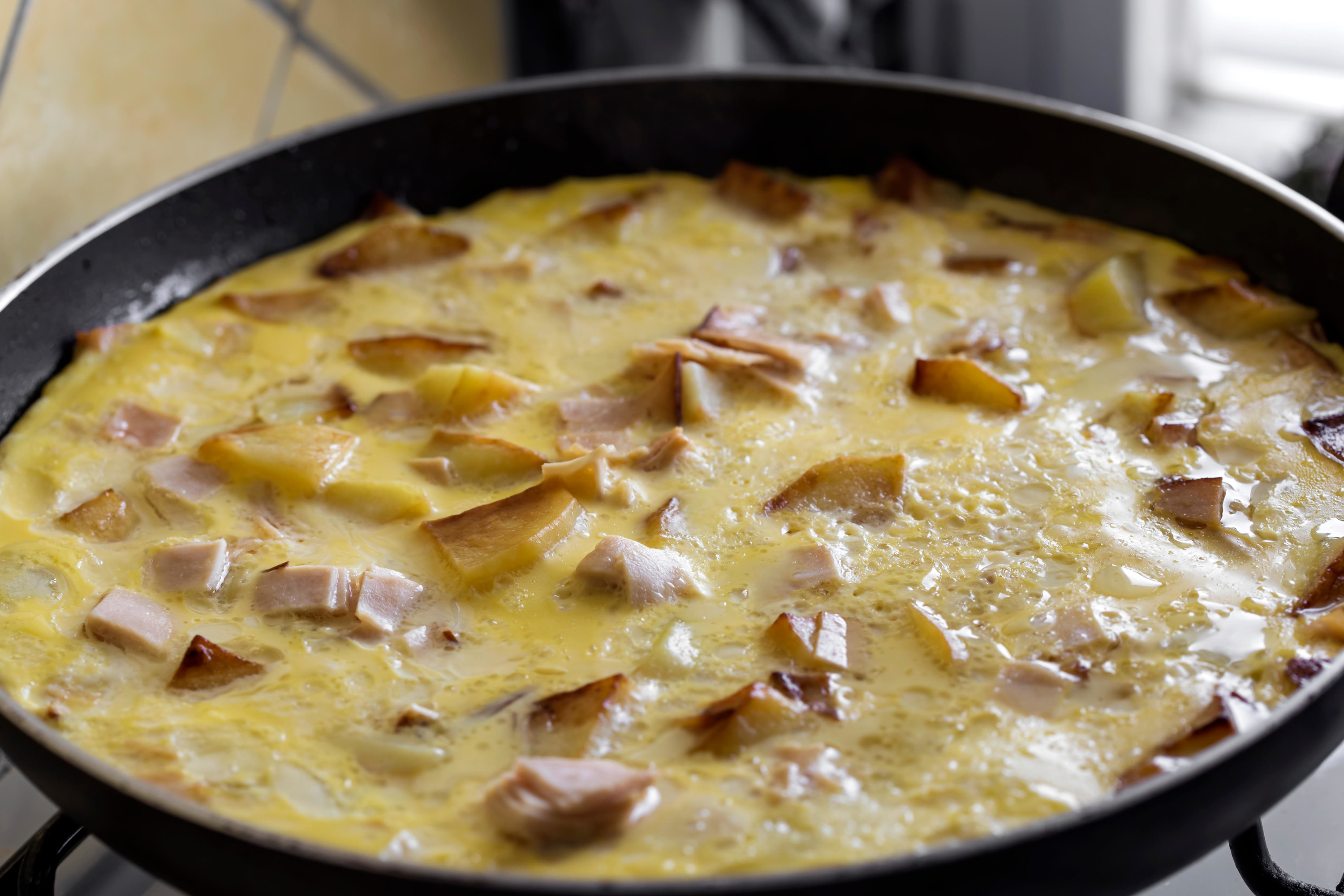 Cooking omelette made with eggs, potatoes and ham in pan