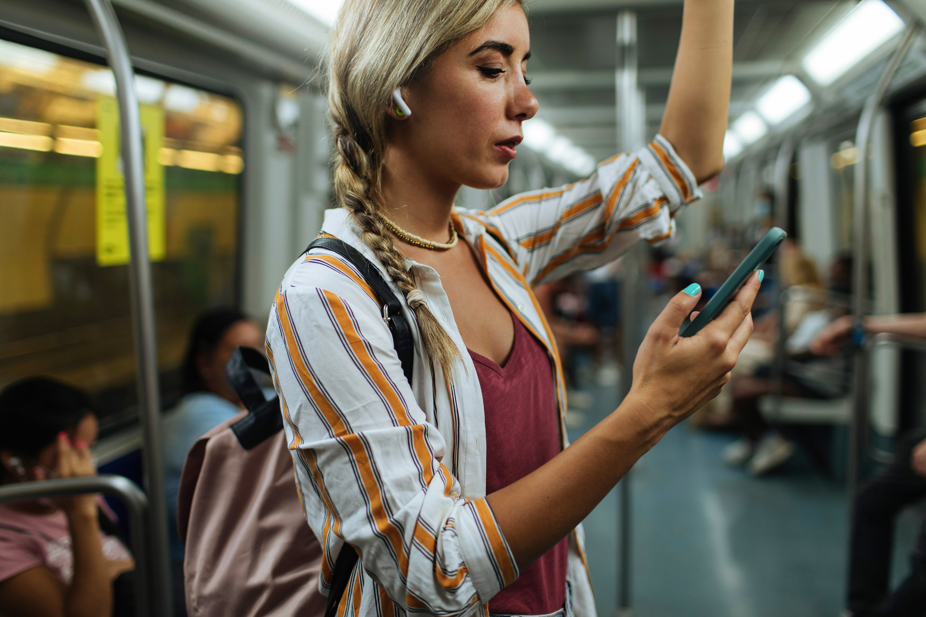 A woman standing in a train car looking on her phone with headphones on