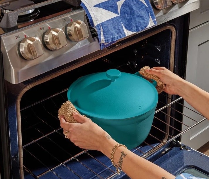teal deep pot with lid being pulled out of the oven by its two side handles