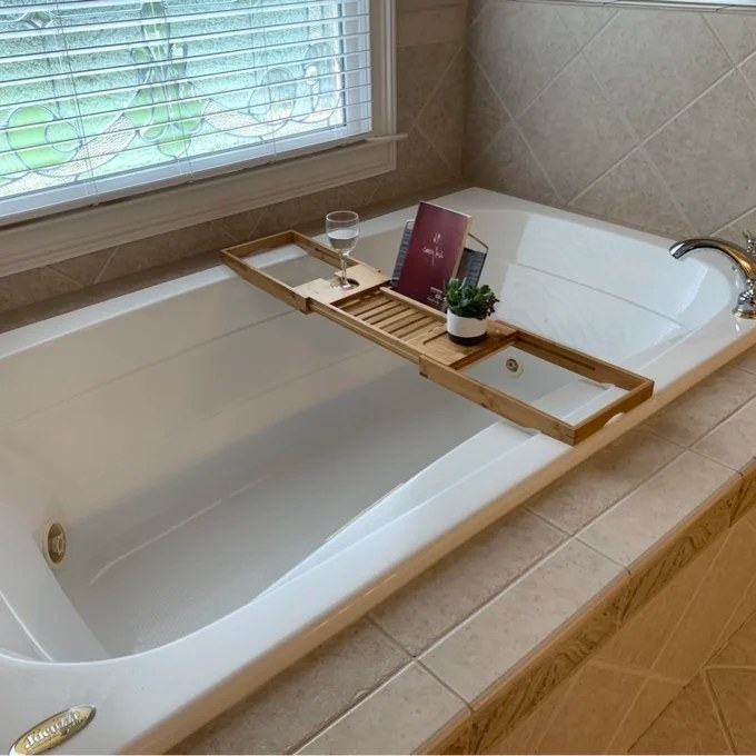 The bath tray with a book, a plant, and a wine glass on it