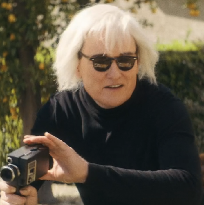 Conan as Andy in a platinum blonde wig and camera in hand