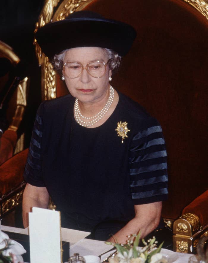 The Queen wearing a brimmed hat, eyeglasses and a three-strand pearl necklace