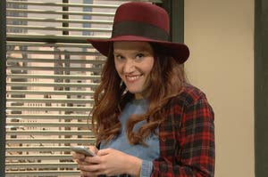 Kate McKinnon smiling while holding a cellphone in an SNL sketch