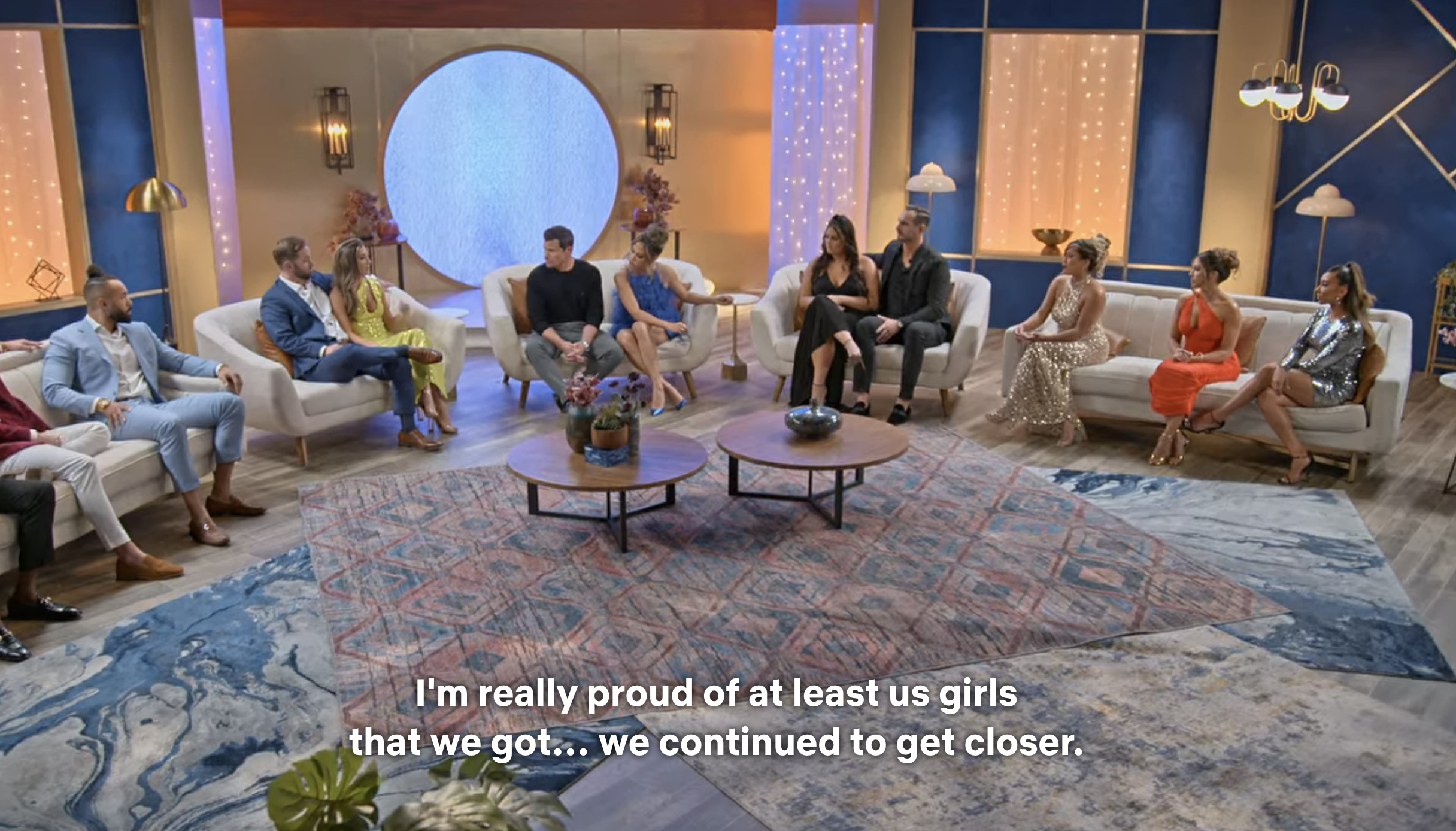 The cast seated in a semicircle, with the caption &quot;I&#x27;m really proud of at least us girls that we got...we continued to get closer&quot;