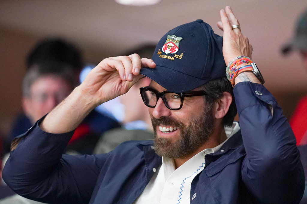 ryan reynolds holding his brim cap and smiling