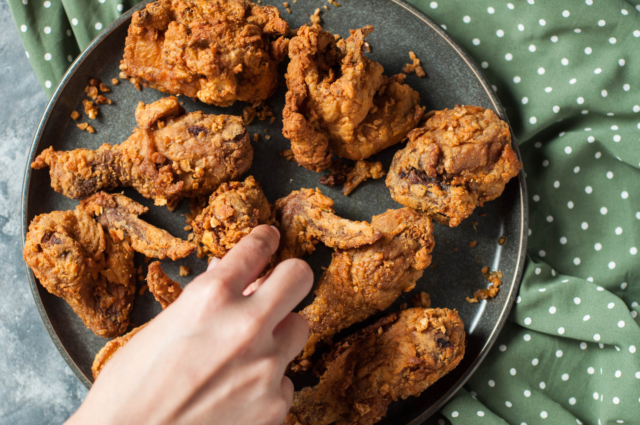 A hand reaching for fried chicken.