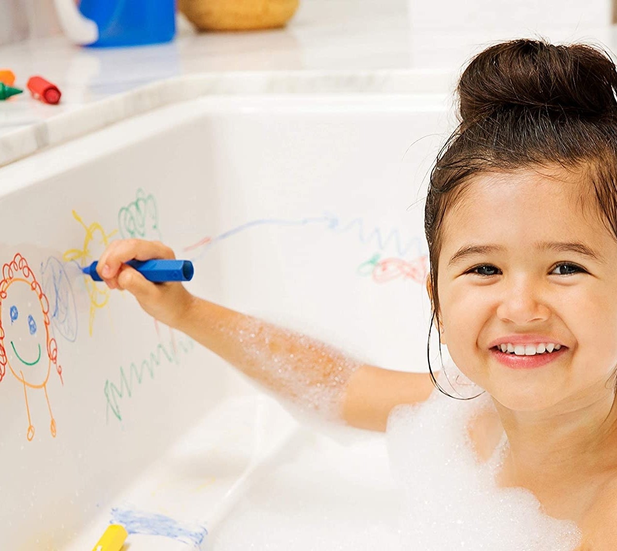 a kid in the bath using the crayons to draw on the tub