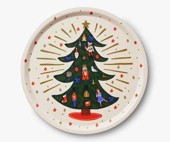 a round off white serving dish with a christmas tree on it and illustrated nutcracker ornaments on the tree