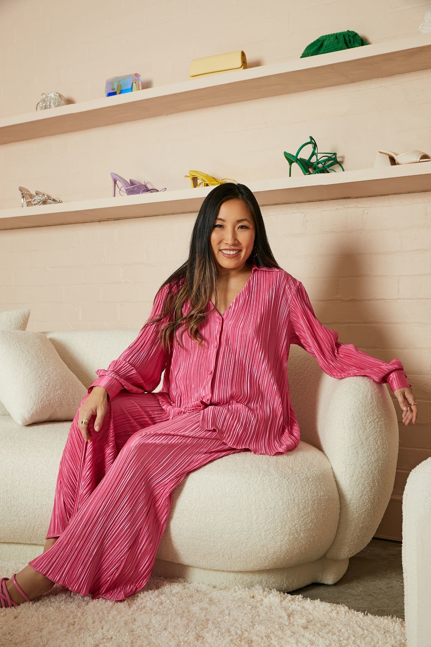 Smiling Jane Lu sits on a couch in a pink outfit