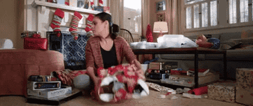 gif from bad moms christmas of Mila Kunis throwing a poorly wrapped present over her shoulder