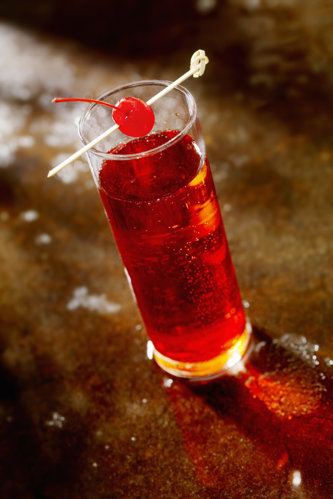 A red drink in a tall glass with a cherry on a stick