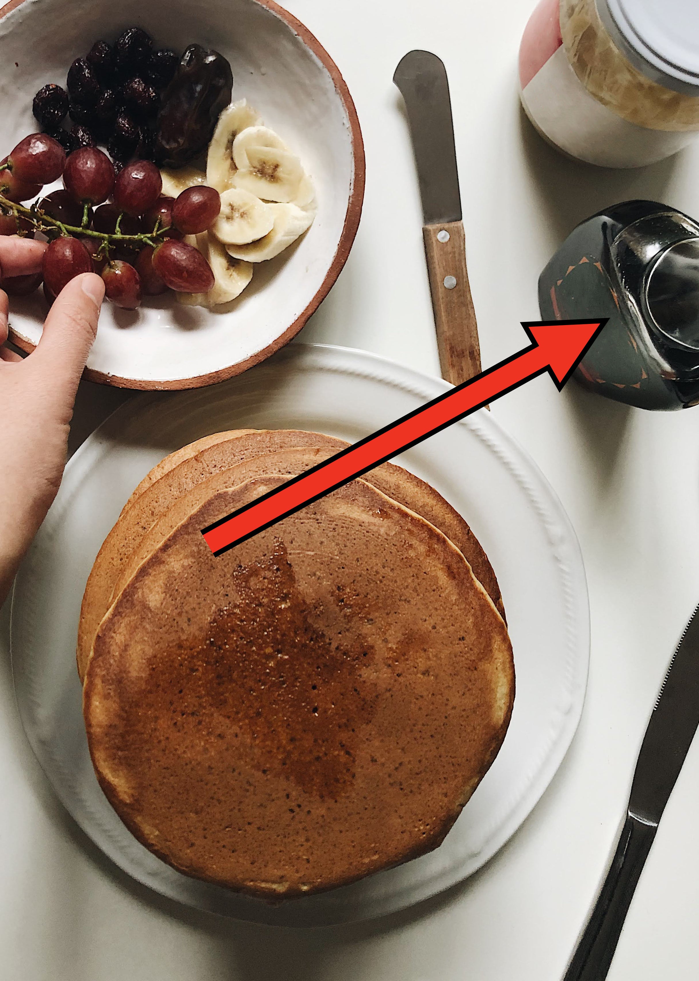 arrow pointing to real maple syrup in a bottle on table with pancakes