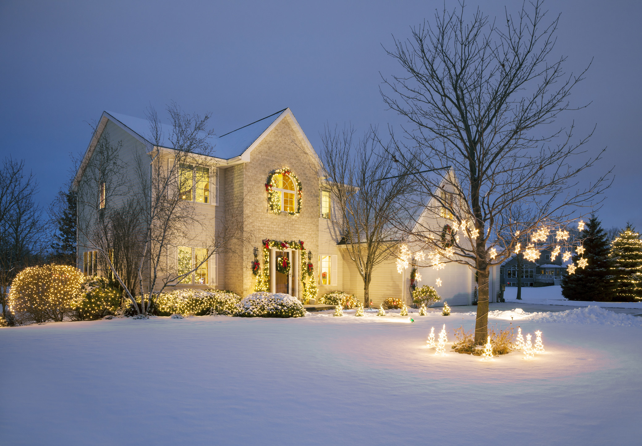 A large house with Christmas lights and surrounded by snow