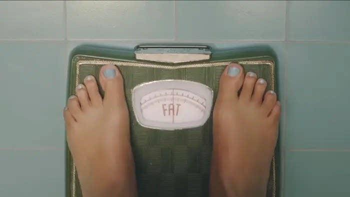 Feet standing on a bathroom scale that has no numbers, it just reads &quot;fat&quot;