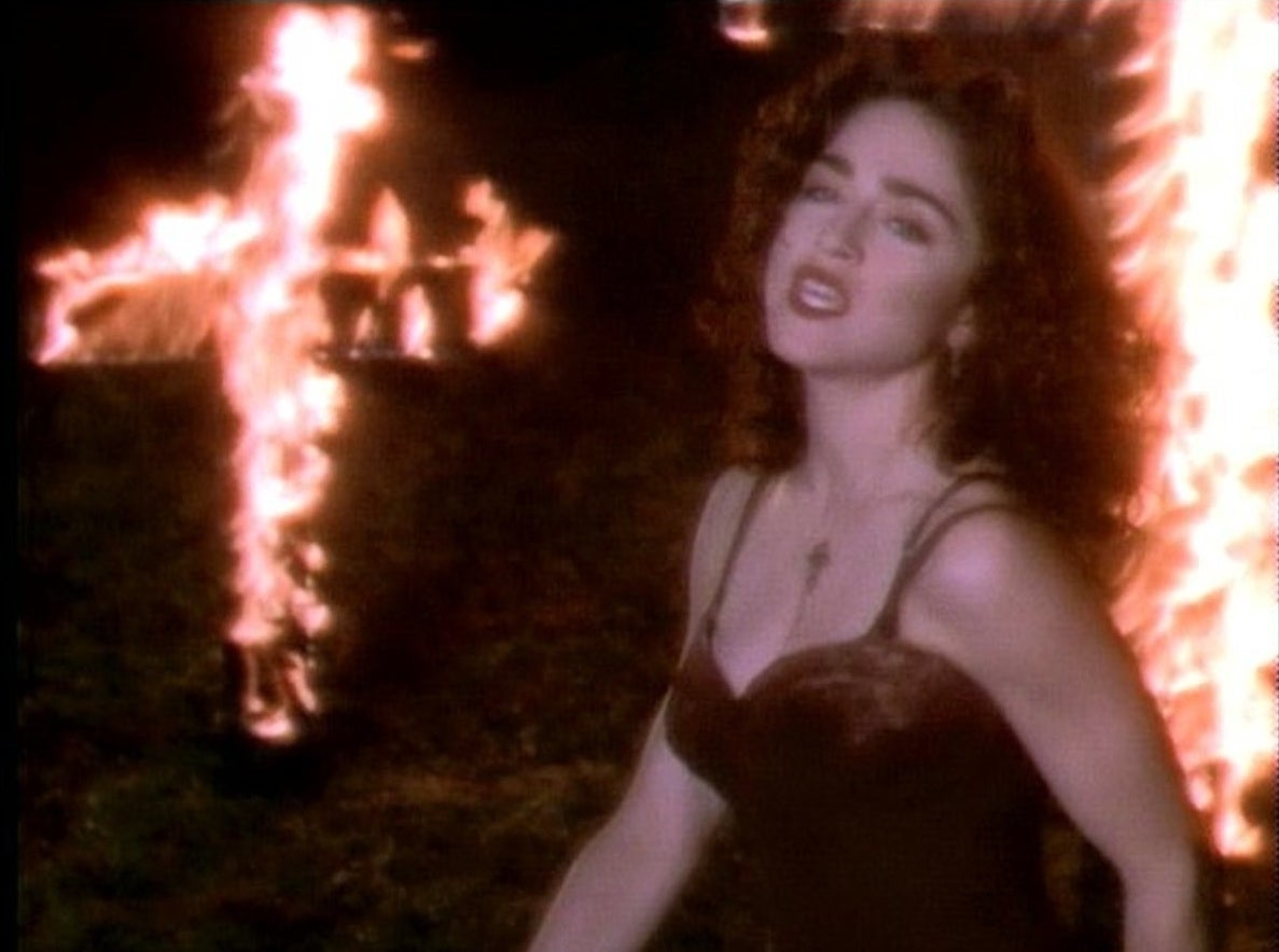 Madonna dancing in a bustier in front of a giant flaming cross