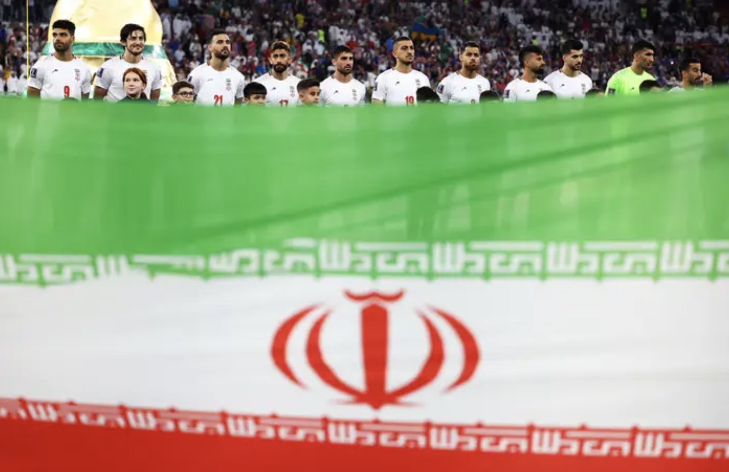 A huge Iranian flag; in the background is a row of Iranian soccer players