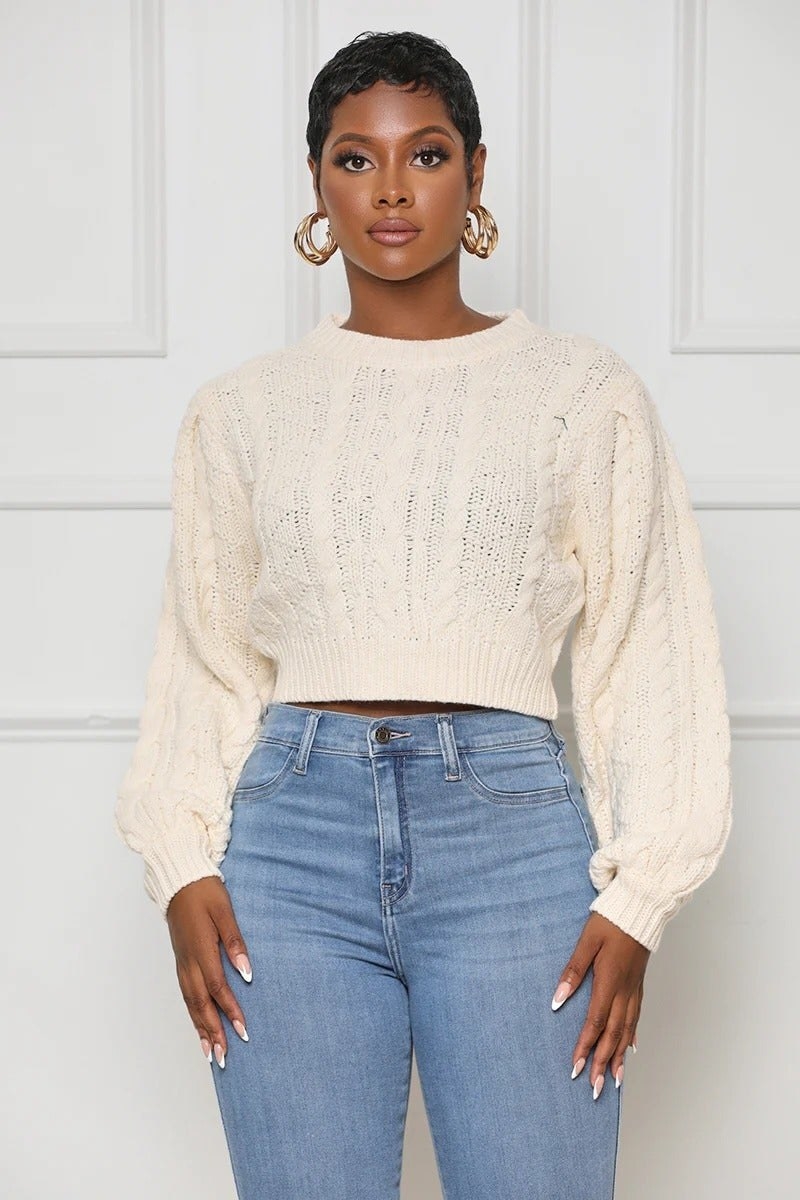 a model wearing a cropped white cable knit sweater with blue jeans