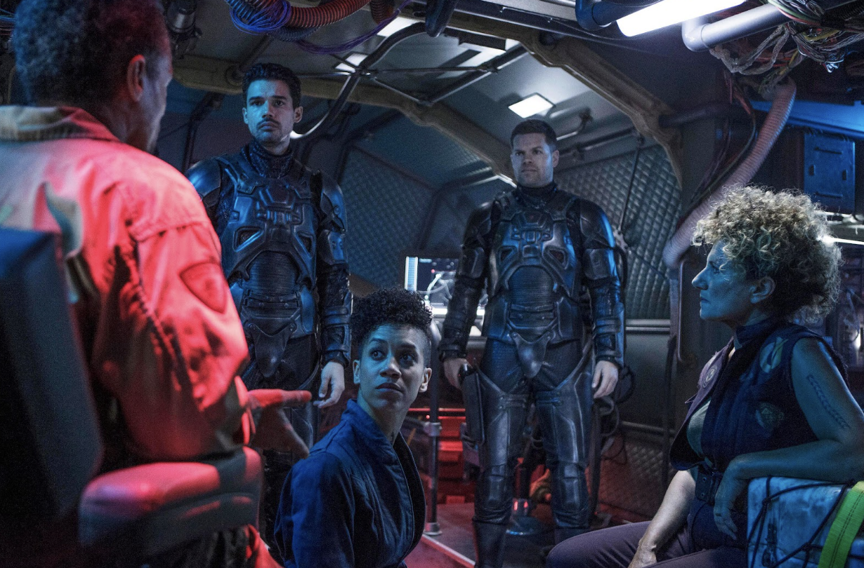 A group of people stand and sit in a spaceship