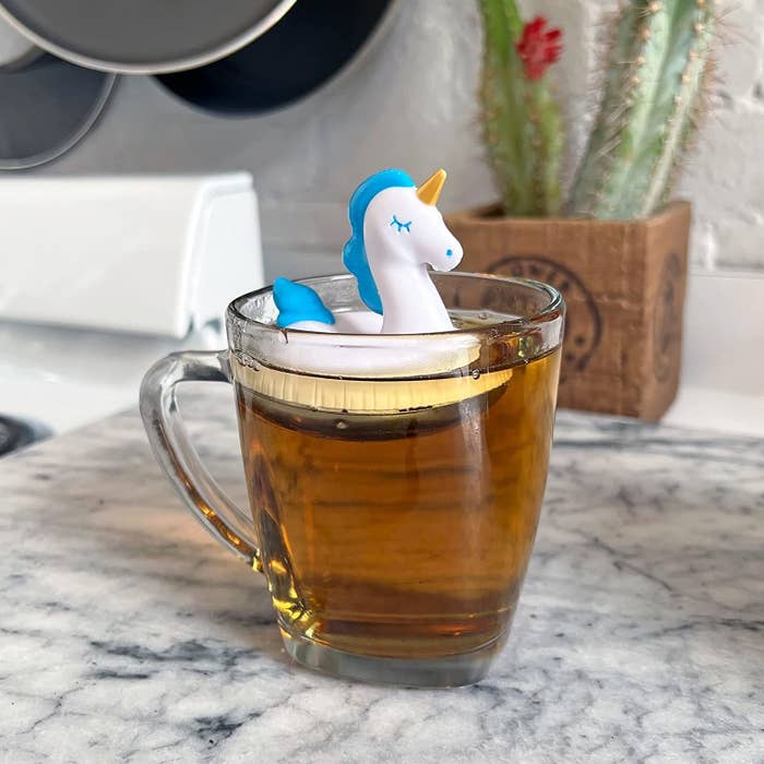 The unicorn shaped tea infuser floating in a cup of tea