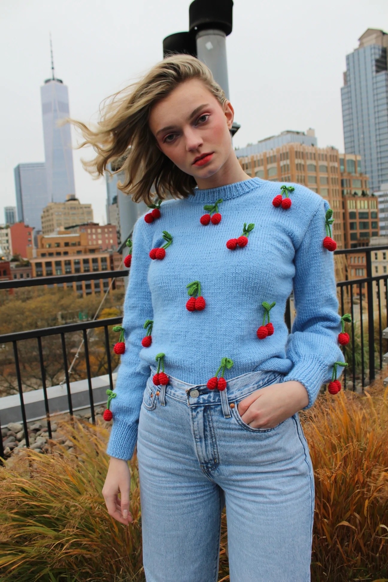 model in light blue sweater with 3D knit cherries all over it