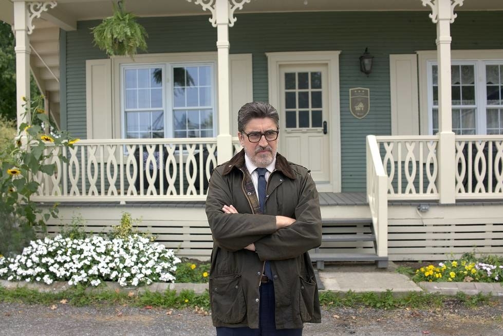 Alfred Molina stands in front of a house