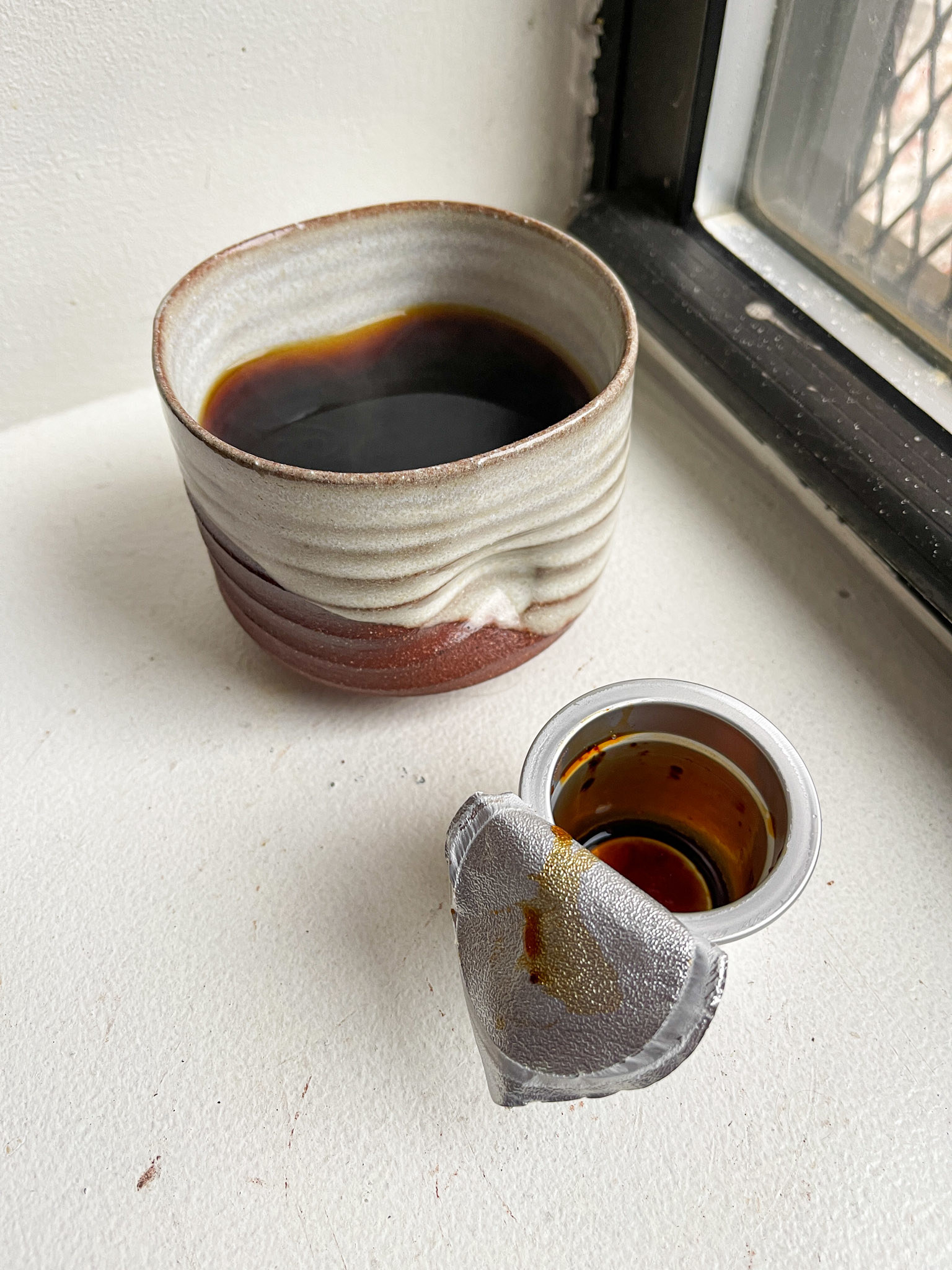 empty coffee capsule next to hot coffee mug