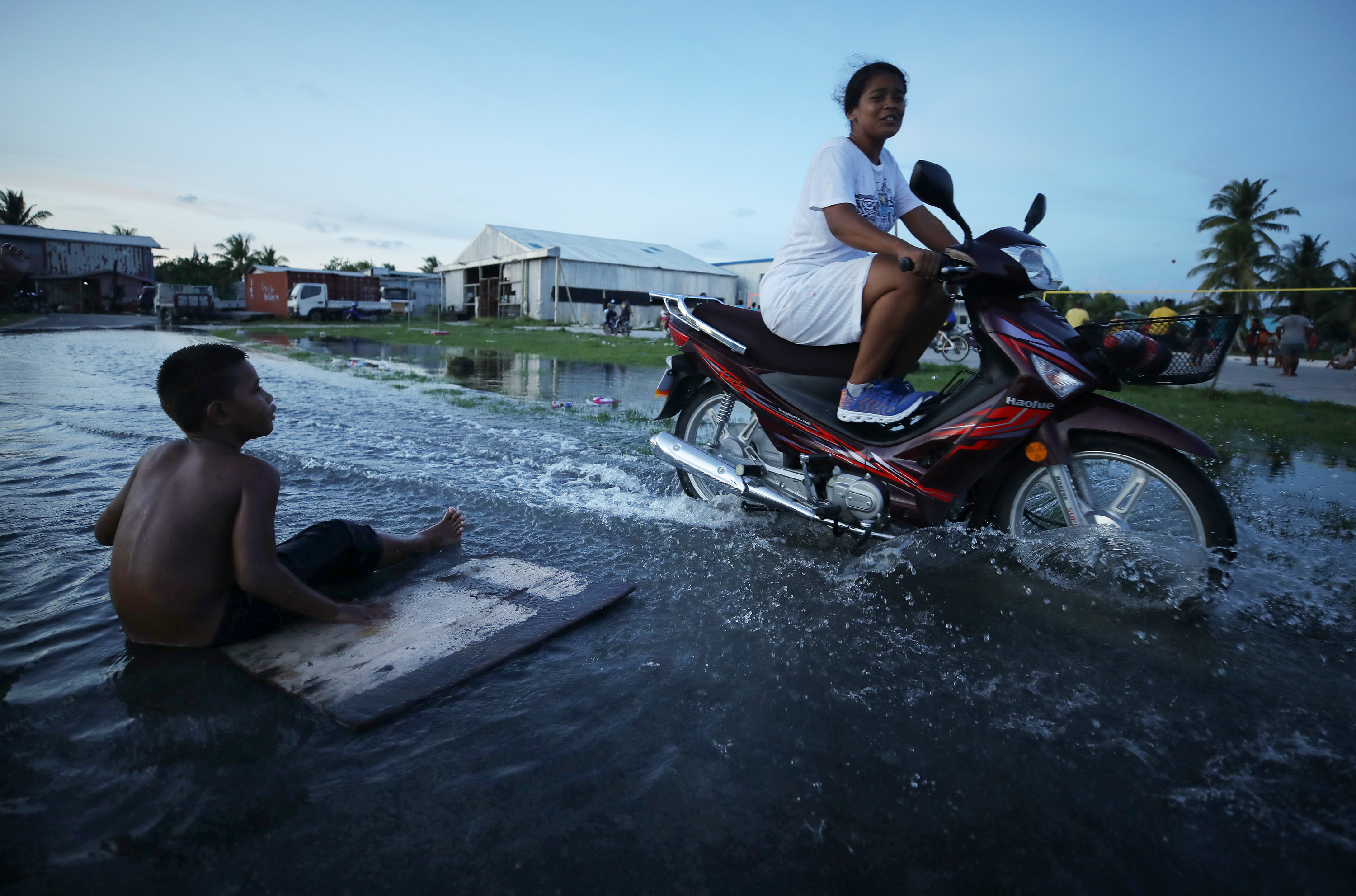 A woman rides a motorbike through flood water in Funafuti, Tuvalu