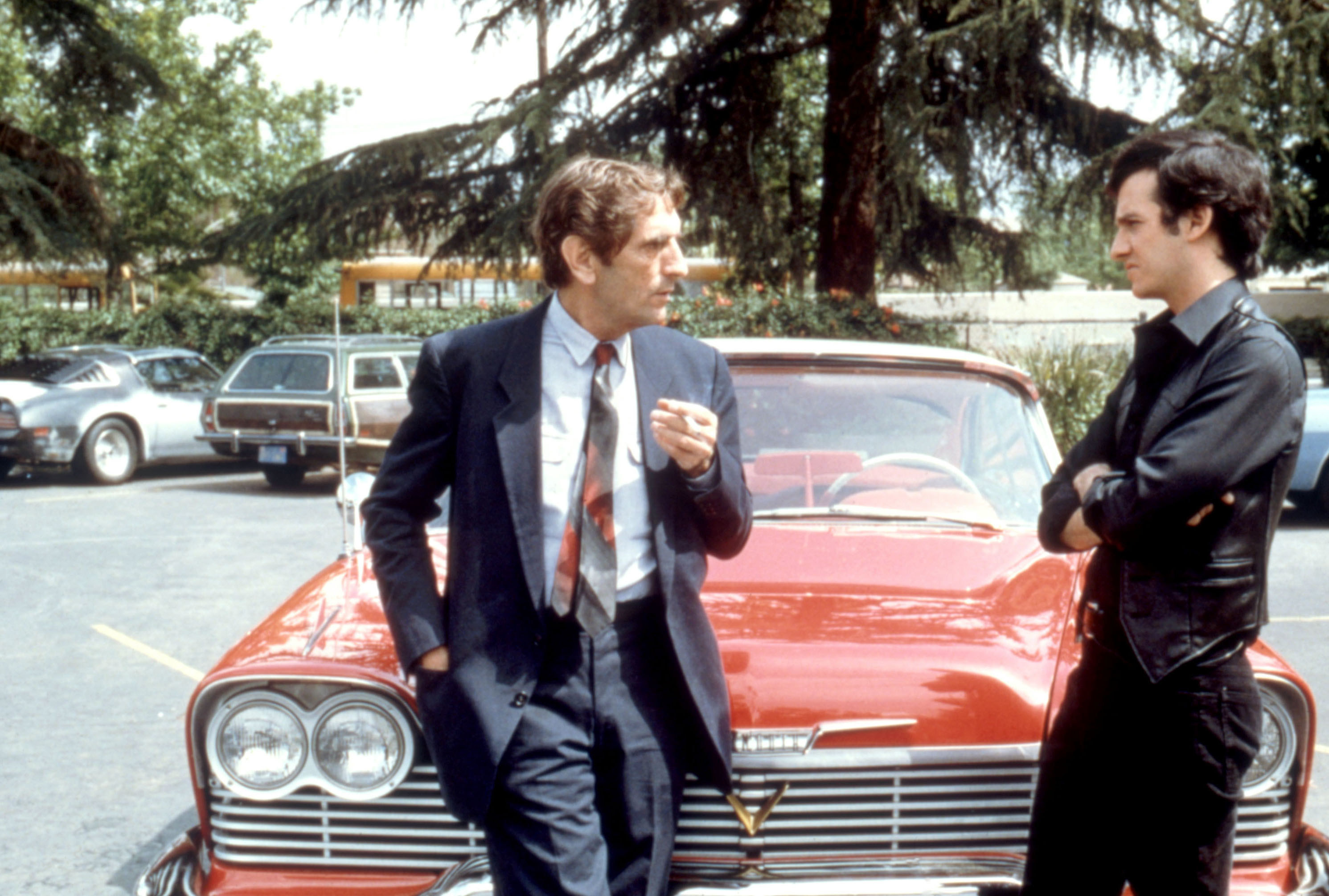 Harry Dean Stanton and Keith Gordon talking by a car.