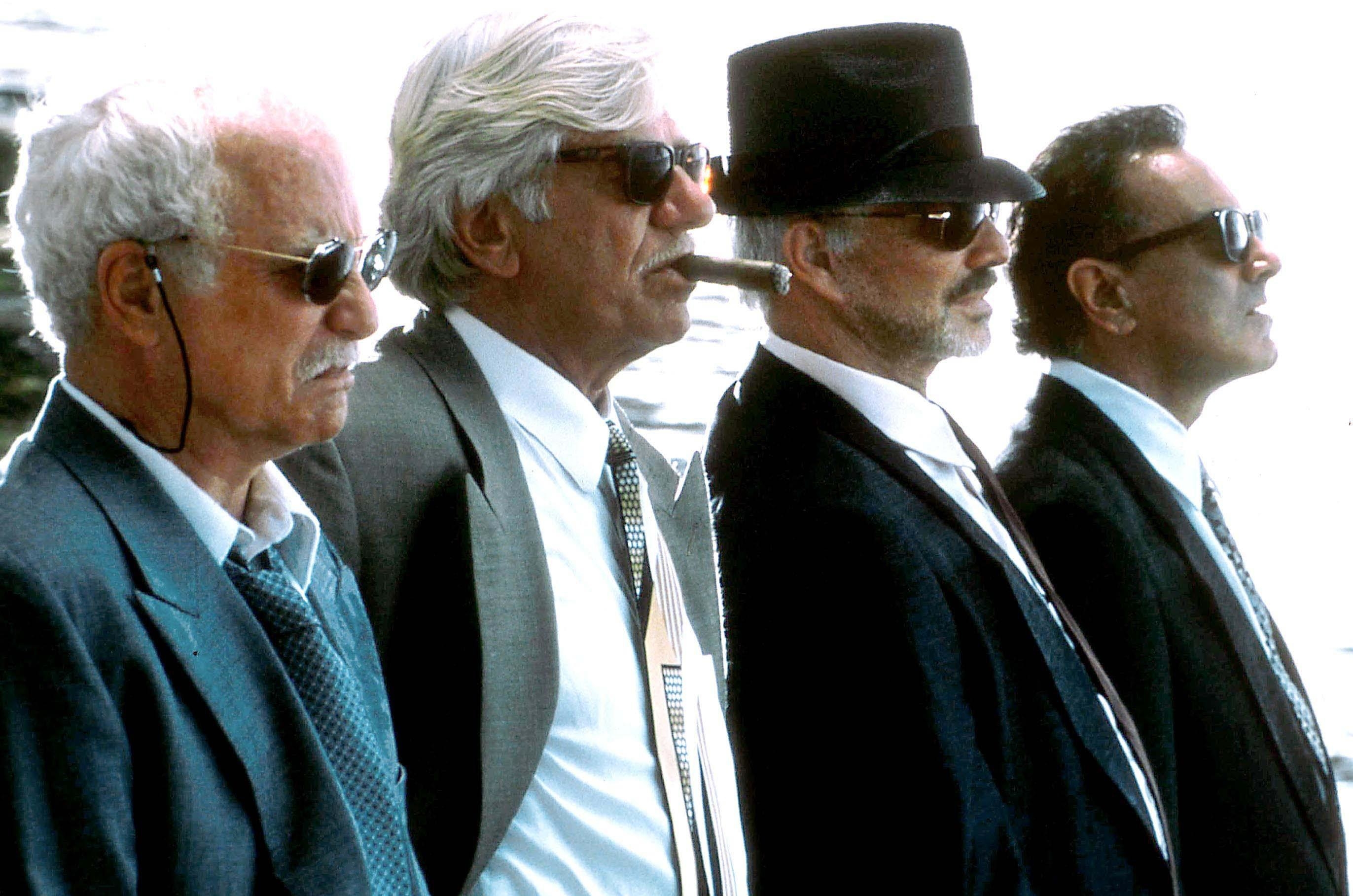 Four sharp-dressed senior men stare with grimaces into the distance