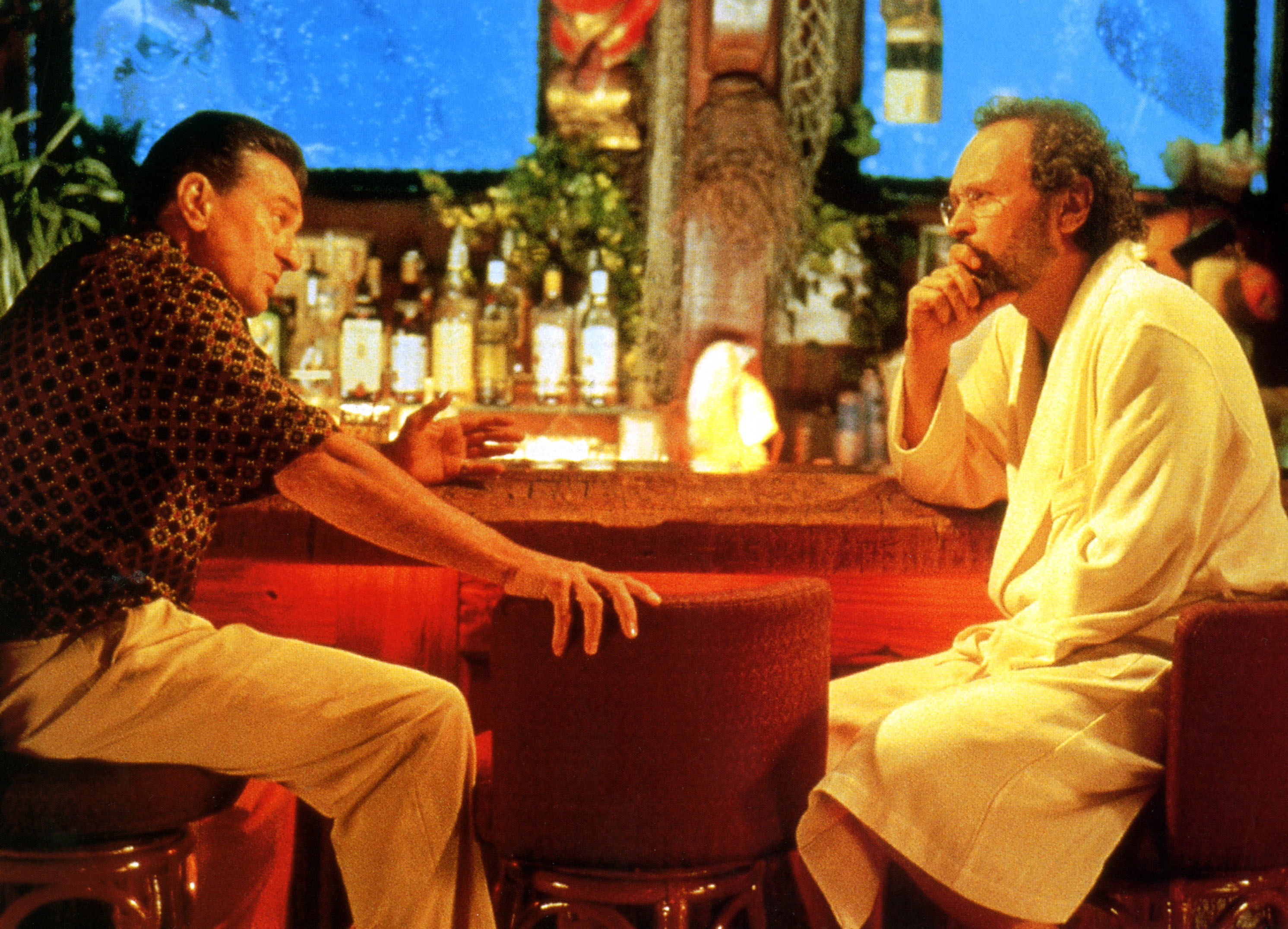 A man in a ornate shirt and khakis sits with a therapist in a long robe
