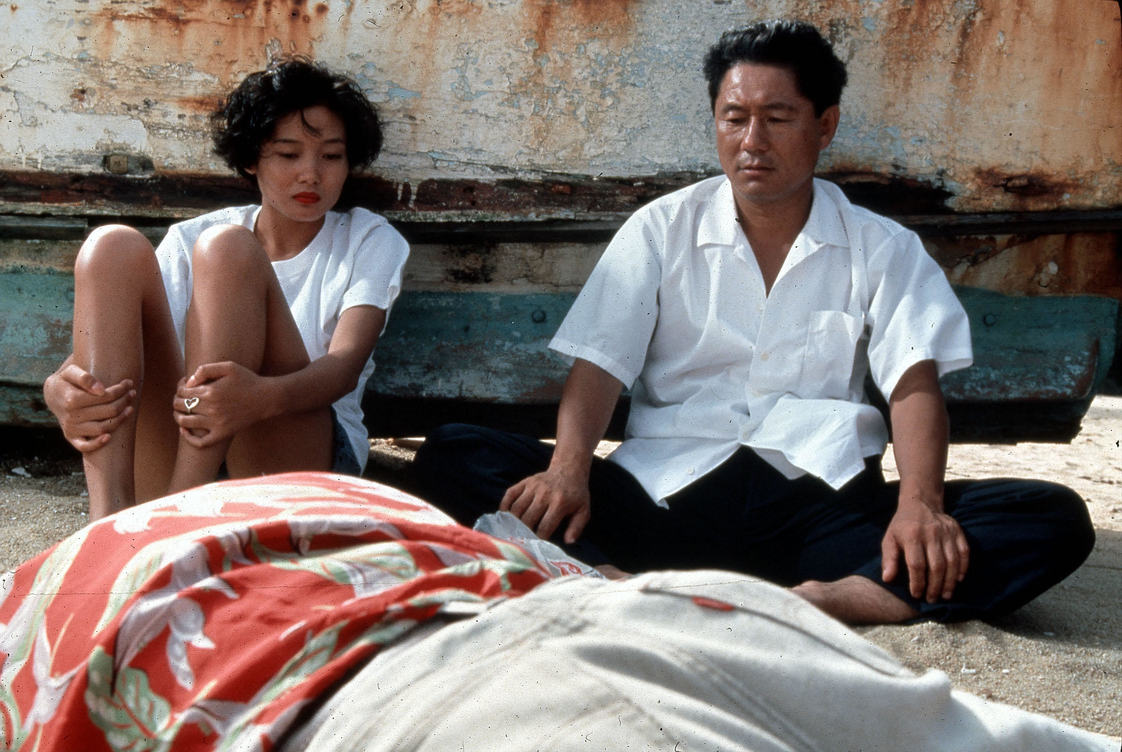 A gangster and his girlfriend observe a dead body near a decrepit boat