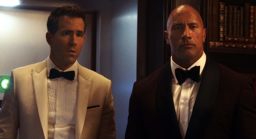 Ryan Reynolds on a white suit standing next to The Rock/ Dawn Johnson