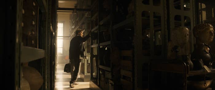 Indiana Jones holding a briefcase and standing in the stacks of a library