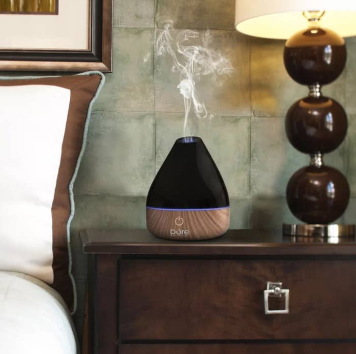 The black diffuser emitting essential oil mist on nightstand table
