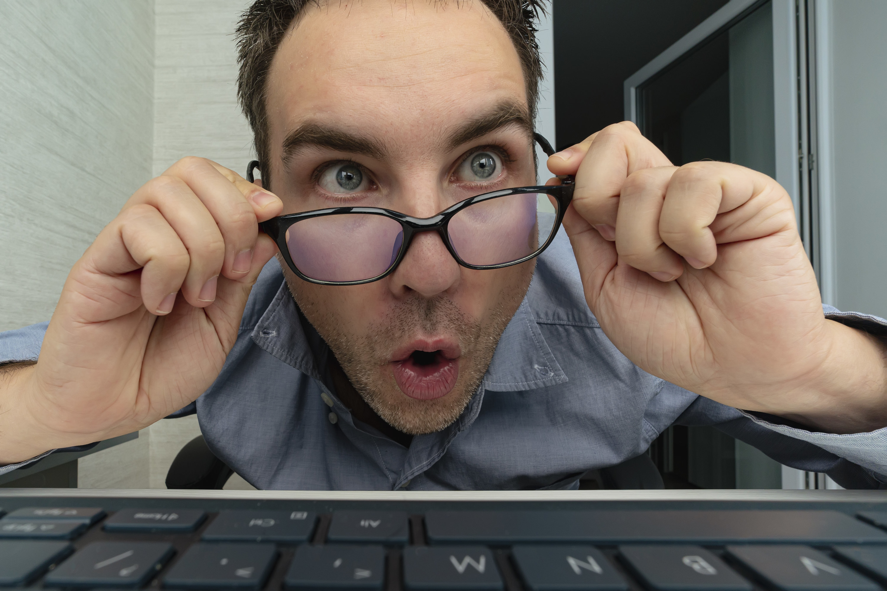 A man hovering over his computer and pulling down his glasses
