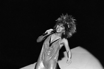 Black and white photo of Tina Turner in shiny dress passionately singing into microphone