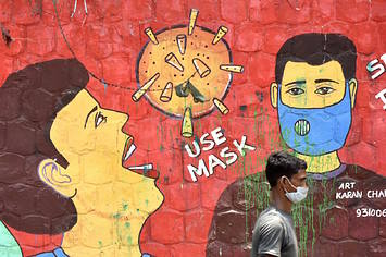 A man wearing a face mask crosses a mural on the use of masks