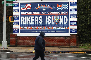 A woman walks by a sign at the entrance to Rikers Island
