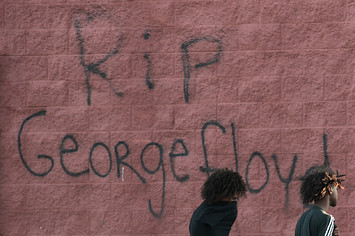 Two men walk past a wall that has "RIP George Floyd" .