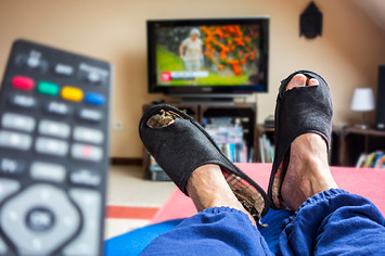 Remote control and couch potato, lazy man in comfy chair wearing worn slippers