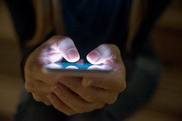 Stock image of a woman using her phone outside at night.