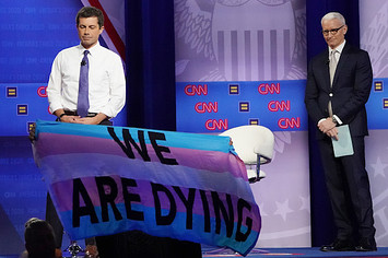 Pete Buttigieg and Anderson Cooper react as protestors display banners.
